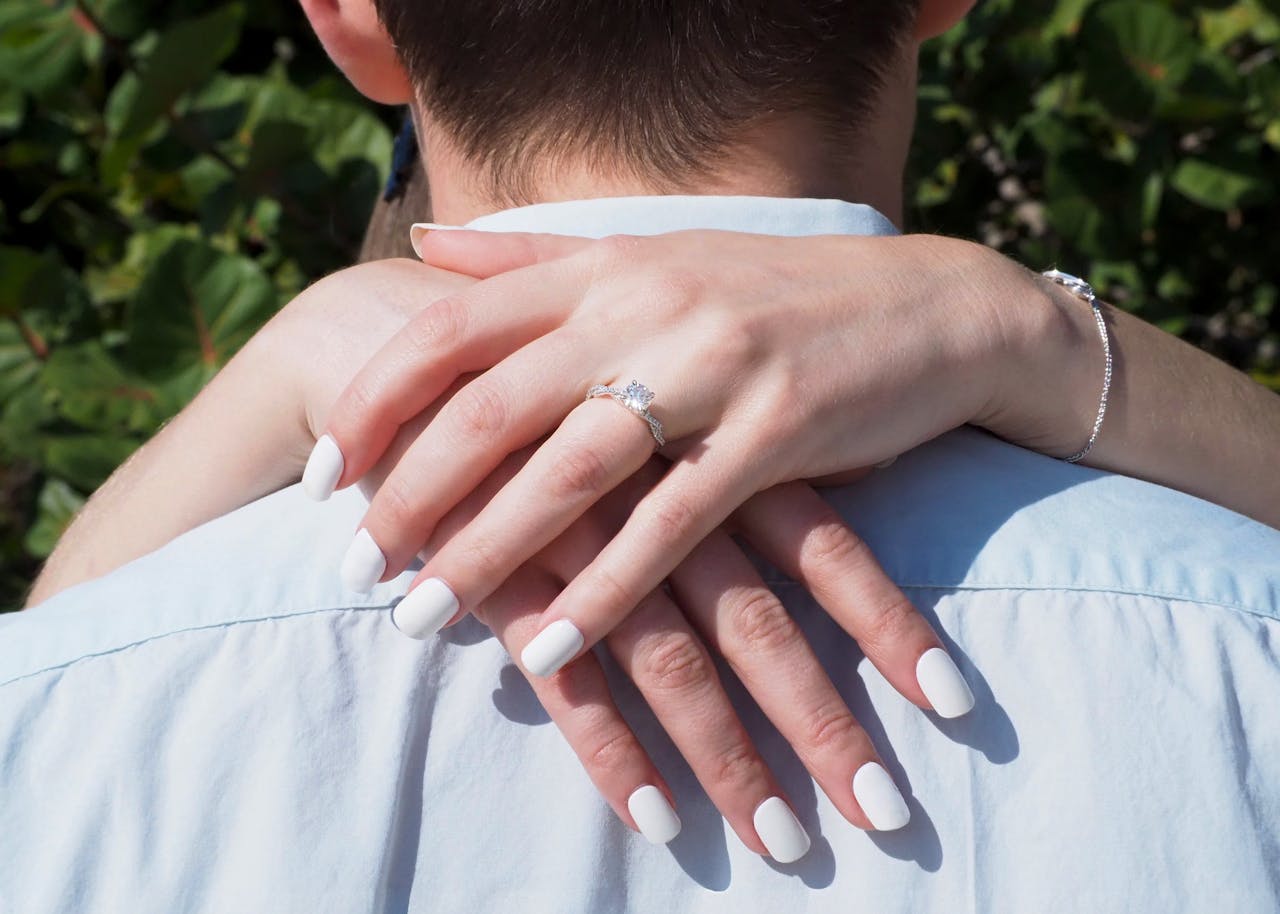 Close-up of a couple embracing, showcasing a diamond engagement ring during a sunny day.